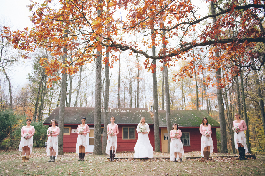 Ginger and her bridesmaids hold their bouquets in front of a bright red cabin with yellow doors and windows at their camp wedding