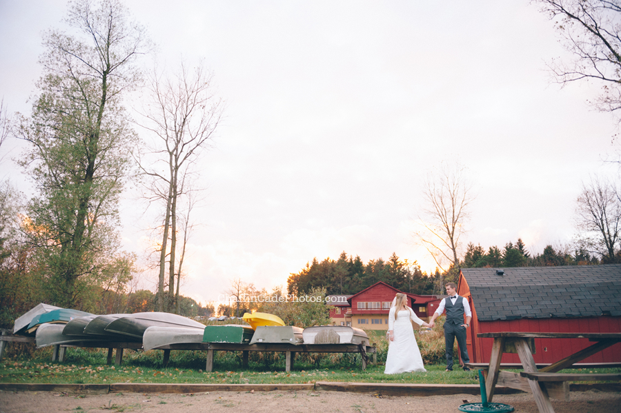 Ginger and Mike stand hand in hand next to colorful and vintage canoes