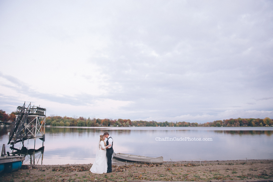 Ginger and Mike stand close in front of the canoe and the lake at camp